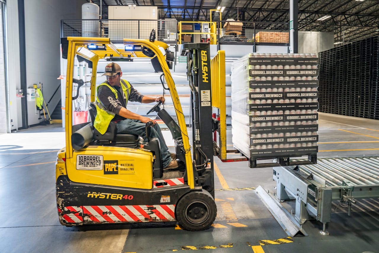 our-services-3 A warehouse worker maneuvers a forklift to transport crates for brewing company storage.