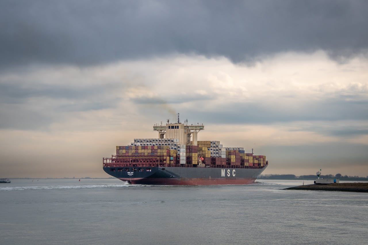 Cargo ship loaded with containers sailing on a calm sea under overcast skies.