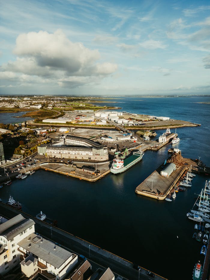 gallery-4 Stunning aerial shot of an industrial harbor in County Clare, Ireland, showcasing ships and coastline under a cloudy sky.
